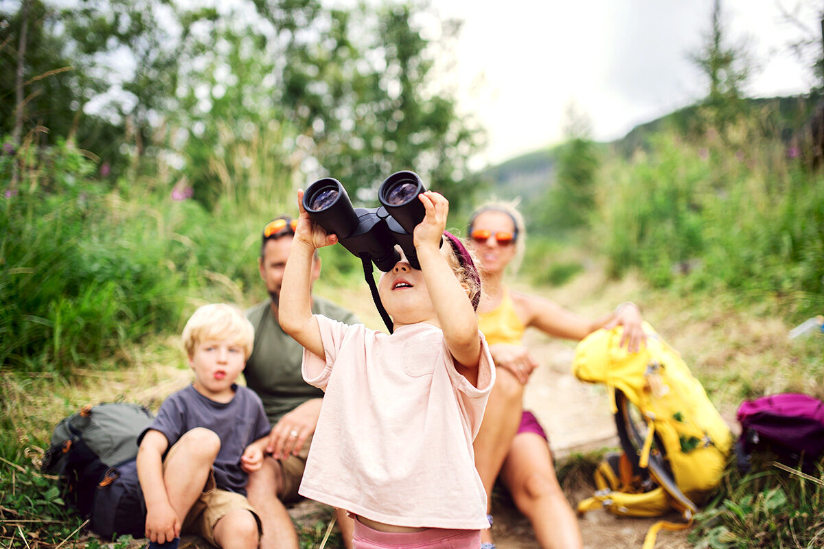 Ein Mädchen mit einem Fernglas beobachtet gemeinsam mit seiner Familie Vögel im Wald.